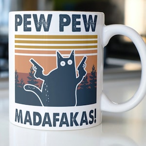 May include: White ceramic coffee mug with a black cat holding two guns and the text "PEW PEW MADAFAKAS!" in a retro style.