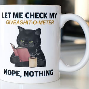 May include: White ceramic mug with a black cat wearing glasses and reading a book. The mug has the text "Let me check my giveashit-o-meter. Nope, nothing."