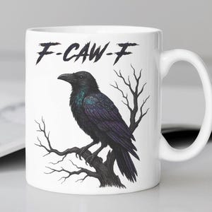 May include: White ceramic mug featuring a detailed illustration of a black raven perched on a tree branch. The mug has the text "F-CAW-F" in a stylized font. The raven has iridescent purple and green feathers.
