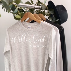May include: A heather grey long-sleeved t-shirt mockup hanging on a wooden hanger. The shirt is tied in a knot at the bottom. The text "Willowbend Mockups" is printed on the shirt.