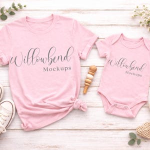 Könnte beinhalten: Ein hellrosa T-Shirt und Baby-Body-Mockup mit dem Text "Willowbend Mockups" in einer Schreibschrift. Das T-Shirt ist unten geknotet. Ein Holzspielzeug liegt zwischen den Kleidungsstücken auf einem weißen Holzgrund.