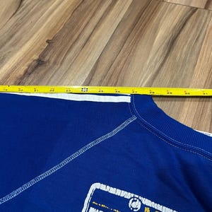 May include: Blue sweatshirt with a white stitched seam and a yellow and white graphic of a Minnesota license plate with the text "Minnesota" and "Gophers".