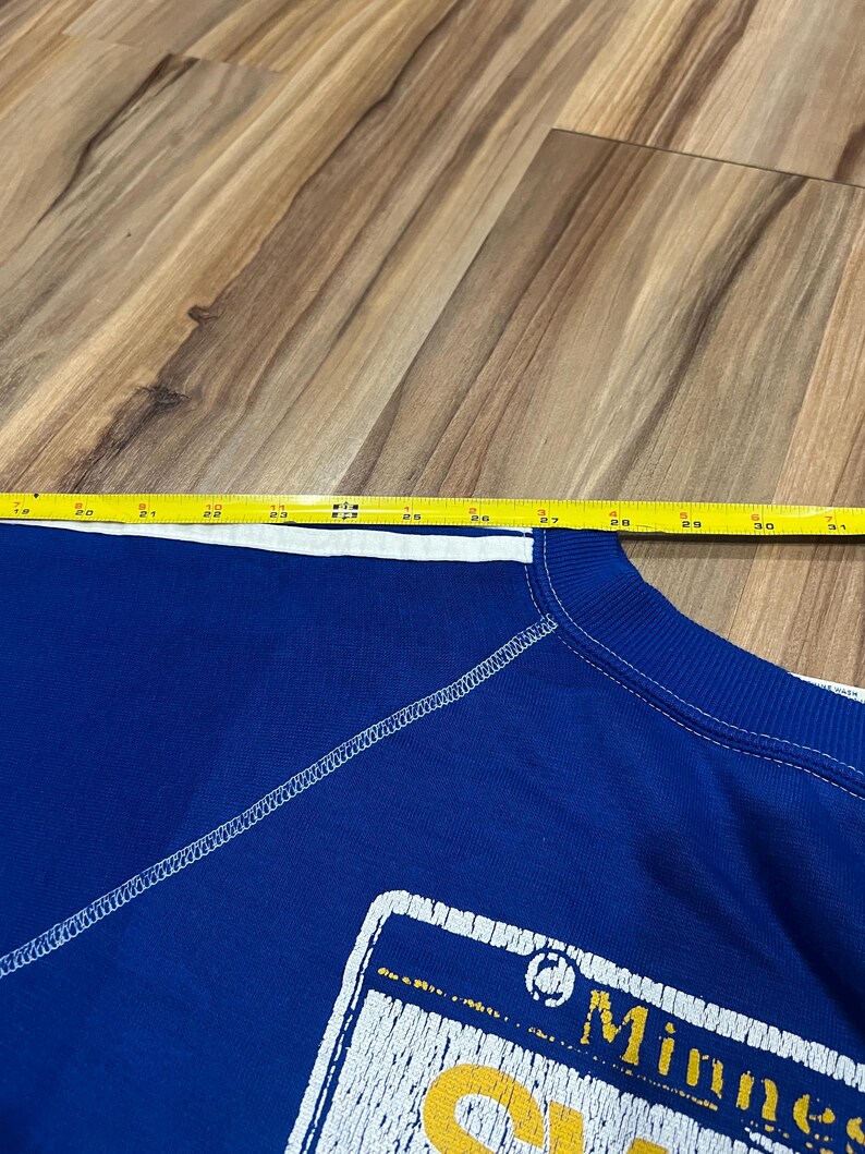 May include: Blue sweatshirt with a white stitched seam and a yellow and white graphic of a Minnesota license plate with the text "Minnesota" and "Gophers".