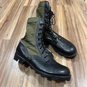 May include: A pair of black and olive green combat boots with black laces. The boots have a leather toe and heel with a canvas upper. The soles are thick and textured.