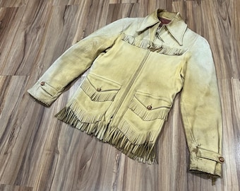 Peut inclure: Veste en daim beige avec des franges sur la poitrine, les poches et l'ourlet. La veste a un col, une fermeture éclair et deux poches avant avec des fermetures à boutons. Les manches ont des poignets boutonnés.