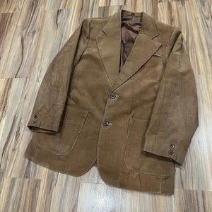 May include: A brown corduroy blazer with a two-button fastening, two front pockets, and buttoned cuffs. The jacket features a notched lapel and a brown satin lining. The blazer is a classic style.