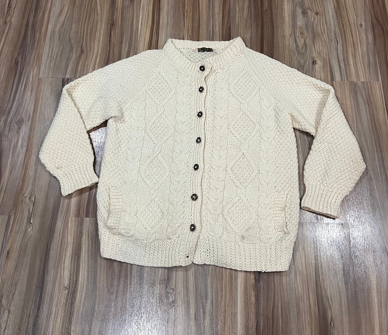 May include: A cream-colored knitted cardigan with a button-up front and a cable knit pattern.