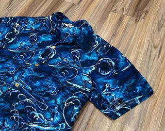 May include: Short-sleeved button-up shirt with a blue and white swirling pattern. The shirt has a classic collar and gold-colored buttons. The fabric appears to be lightweight, suitable for warm weather.