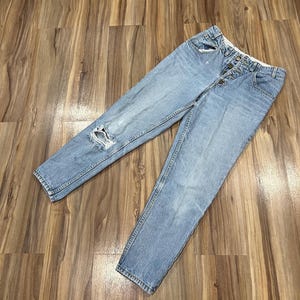 May include: Light blue denim jeans with a distressed knee and a button fly.