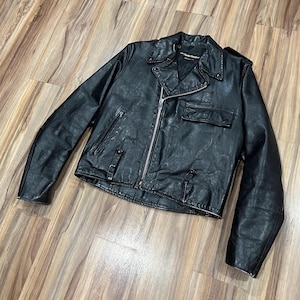 May include: A black leather motorcycle jacket featuring a silver-tone asymmetrical front zipper, a notched lapel collar with snap buttons, a zippered chest pocket, a flap pocket on the front, and long sleeves with a textured, worn-in finish.