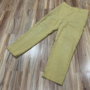 May include: A pair of yellow plaid pants. The pants have a classic fit with a button and zipper closure. The fabric has a subtle grid pattern in a darker shade of yellow.