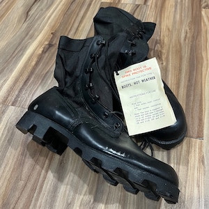 May include: A pair of black leather military boots with a tag that reads "This boot is spike protective instruction tag for type 1 boots, hot weather".