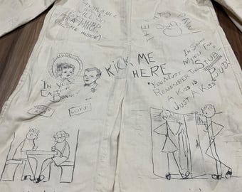 May include: A long-sleeved off-white coat featuring various hand-drawn black ink illustrations and text, including phrases like "Kick Me Here," "Jellyin'," "Jawin'," and "In Your Easter Bonnet," along with cartoon sketches of people and objects.