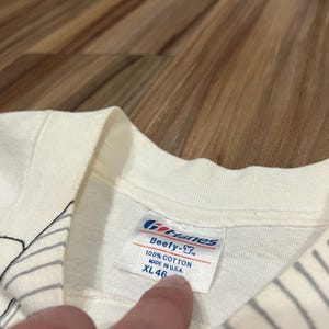 May include: Close-up of a white t-shirt tag. The tag reads "Gildan Beefy-T", "100% Cotton", and "Made in U.S.A.". The size is XL 46.