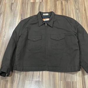 May include: A dark gray work jacket with a zipper closure and two large pockets on the front. The jacket has a label that reads "DAN RIVER" on the collar.