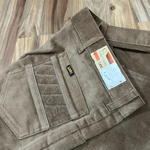 Puede incluir: Primer plano de pantalones de pana marrones con un diseño de bolsillo texturizado. Los pantalones tienen una etiqueta Lee y una etiqueta de "The KC Collection by Lee". Los pantalones están doblados y parecen sin usar.