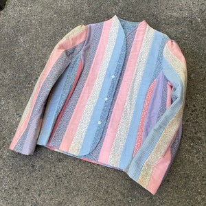 Może przedstawiać: Kurtka pikowana w pasy w kolorze różowym, niebieskim i białym. Kurtka zapinana na guziki i z kołnierzem.