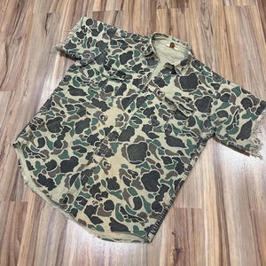Op de afbeelding: Een kort mouw overhemd met knopen in camouflage print met een rafelige zoom. Het overhemd is gemaakt van een lichtgewicht katoenen stof en heeft een ontspannen pasvorm.