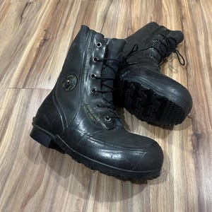 May include: Pair of black rubber boots with a lace-up design. The boots have a rounded toe and a thick sole. Text on the side reads "KEEP DOUBLE LACED TO HOLD FIRMLY". The boots are designed for cold weather.