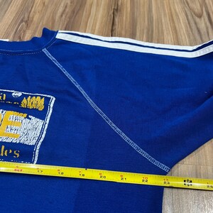 May include: Blue sweatshirt with white stripes on the sleeves and a yellow and white graphic on the front that says "Jes" and "Ups".