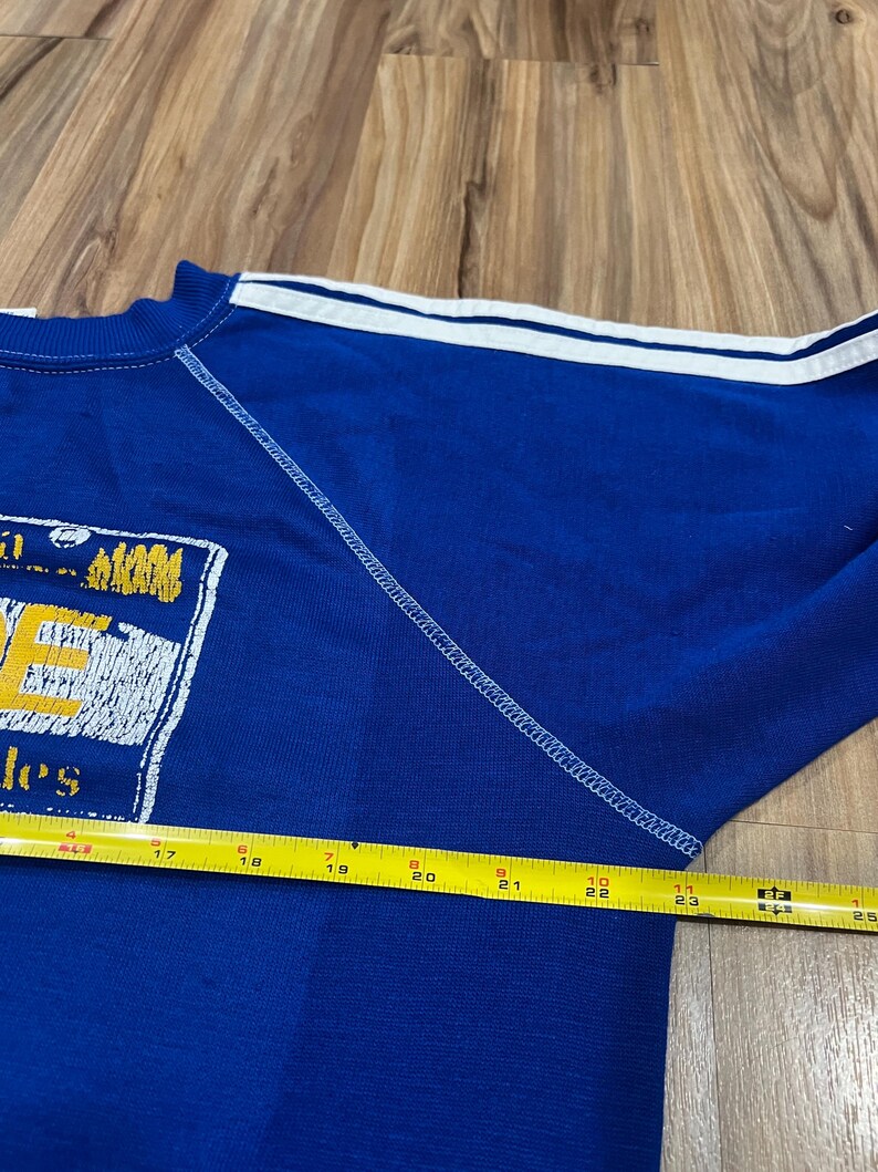 May include: Blue sweatshirt with white stripes on the sleeves and a yellow and white graphic on the front that says "Jes" and "Ups".