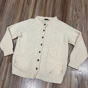 May include: A cream-colored knitted cardigan with a button-up front and a cable knit pattern.