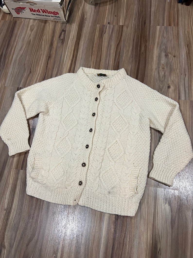 May include: A cream-colored knitted cardigan with a button-up front and a cable knit pattern.