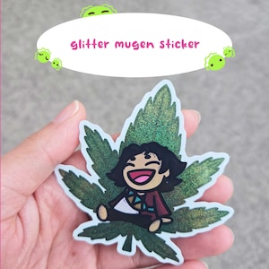 May include: A glitter sticker featuring a cartoon character sitting on a green cannabis leaf. The sticker has a white border and the text "glitter mugen sticker" in pink. The character has black hair and is wearing a red and brown outfit.
