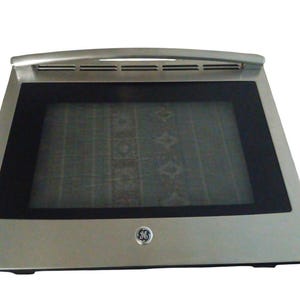 May include: Stainless steel oven door with a black glass window. The door has a handle at the top and a GE logo on the bottom right. The oven door is rectangular and appears to be new.