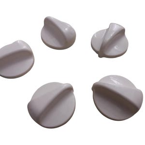 May include: Five white stove knobs with a rounded design and a curved handle. The knobs are made of a smooth, glossy material and are arranged in a scattered pattern against a white background.