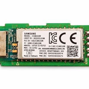 May include: A green rectangular printed circuit board featuring a central metallic shield with a white label. The label displays Samsung branding, model CCAR210R, FCC ID A3LCCAR210R, serial number 900AWJ4NR02120917R, and MAC addresses 50FDD5B2D074 and 50FDD5B2D075.