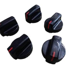 May include: Five black appliance knobs with a red indicator line. The knobs have a ridged design for grip and are likely used for controlling the settings on a stove or oven. The knobs are made of a glossy plastic material.