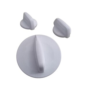 May include: Three white appliance knobs. One large, round knob with a raised handle and two smaller, triangular knobs. All knobs are made of a smooth, solid white material and are set against a plain white background.