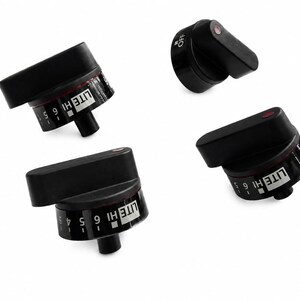 May include: Four black stove control knobs with a cylindrical base and a protruding handle. Each knob features white printed text including the words OFF, LITE, HI, and numbers 1 through 6, along with a small red indicator dot on the top surface.