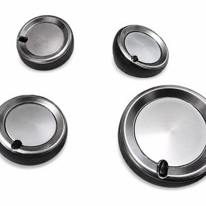 May include: A set of four circular control knobs featuring a brushed silver metallic center disc surrounded by a black plastic base. Each knob includes a small black indicator mark on the outer rim, designed for stove or appliance operation.