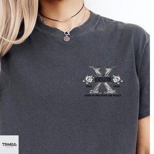 Pu&ograve; includere: Una maglietta grigia scura con una grafica in stile vintage di una grande lettera X con il testo "Generation X 1965-1980 Raised on Rose Water and Neglect".