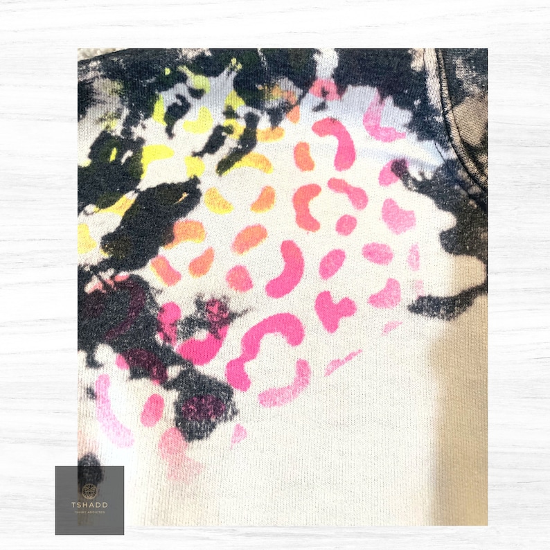 K&ouml;nnte beinhalten: Ein wei&szlig;er Stoff mit einem schwarzen, rosa, orangefarbenen und gelben Batik-Muster. Das Muster zeigt ein Leopardenmuster.