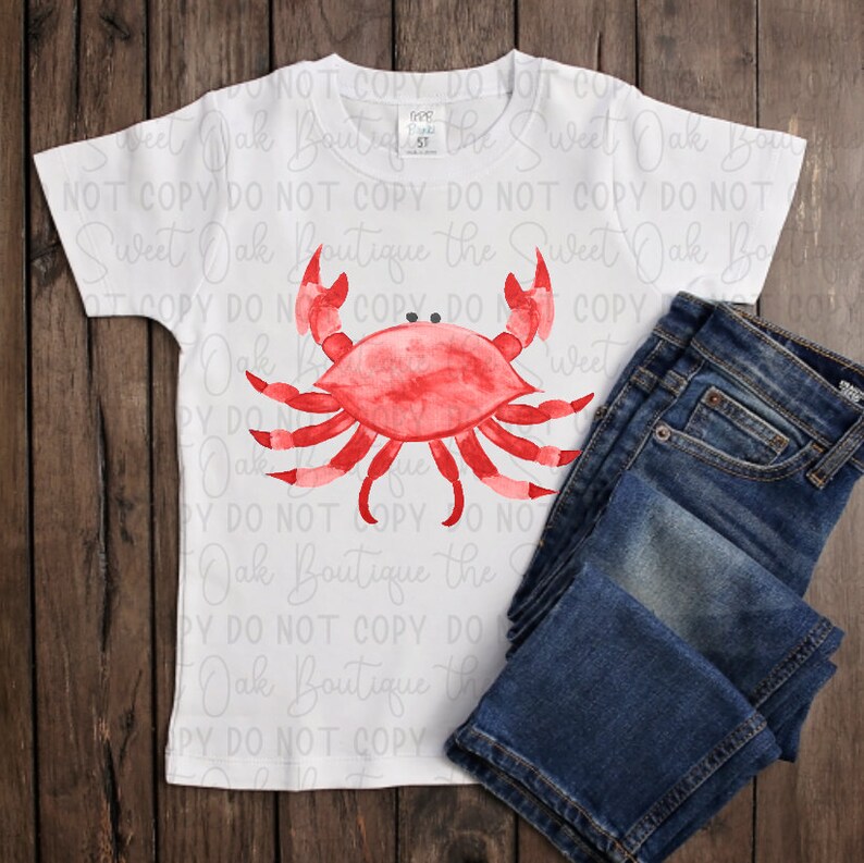 May include: A white t-shirt with a red watercolor crab design. The shirt has the text "Sweet Oak Boutique the Sweet Oak Bo" repeated on it.