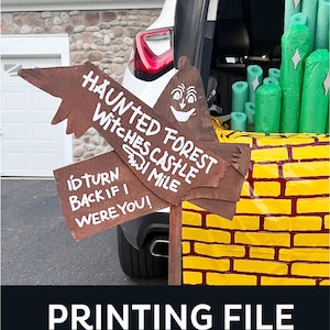 May include: A Halloween-themed display with a brown wooden sign pointing towards a "Haunted Forest" and "Witches Castle." The sign has a smiling face and the text "I'd turn back if I were you!" A yellow brick road and green decorations are visible.