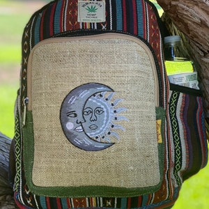 May include: A brown hemp backpack with a multi-colored striped pattern. The front pocket features an embroidered design of a sun and moon with faces. The backpack has a label that reads "Himalaya Hemp THC Free Made in Nepal".