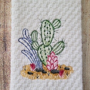 Puede incluir: Toalla de cocina bordada con fondo blanco y un dise&ntilde;o de cactus verde con flores rosas y hojas azules.
