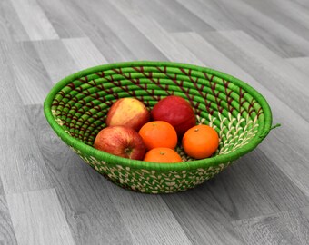 Puede incluir: Una cesta tejida verde con un patrón rojo y verde contiene cinco piezas de fruta: tres manzanas rojas y dos mandarinas naranjas.