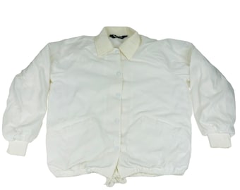 May include: Cream-colored jacket with a light beige collar and cuffs. The jacket has a button-up front, two front pockets, and a drawstring at the bottom. The sleeves are long and slightly puffed. The jacket is made of a smooth, possibly nylon, material.