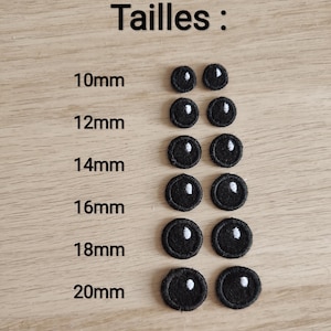 Pode incluir: Conjunto de olhos de feltro preto em vários tamanhos, que vão de 10 mm a 20 mm. Os olhos têm uma pupila branca e estão dispostos em filas sobre uma superfície de madeira.