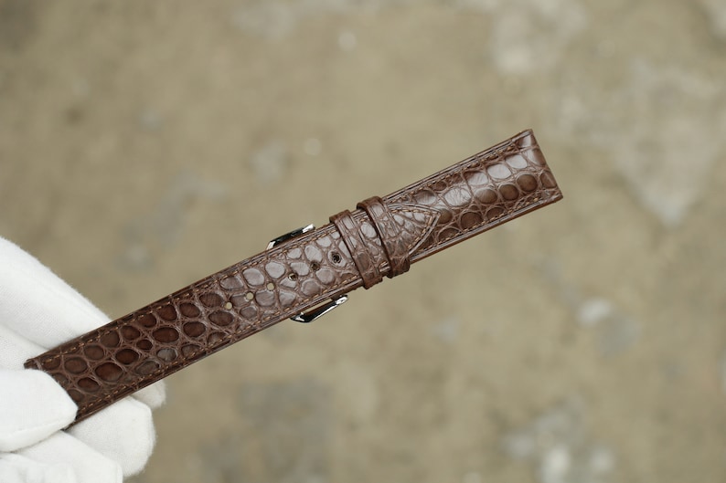 Peut inclure: Un bracelet de montre en cuir marron avec un motif crocodile.