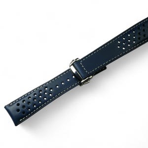 May include: A dark blue leather watch strap with white stitching and a perforated design. The strap has a silver buckle.