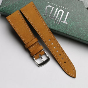 Könnte beinhalten: Ein braunes Lederarmband mit weißen Nähten und einer silbernen Schließe. Das Armband liegt auf einer grünen Box mit dem Text "Tuis Leather Strap".