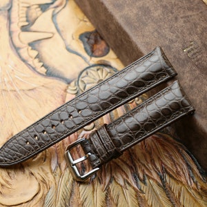 Peut inclure: Deux bracelets de montre en cuir marron avec un motif crocodile. Les bracelets sont sur un fond en cuir marron.