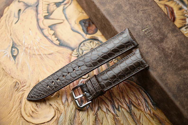 Peut inclure: Deux bracelets de montre en cuir marron avec un motif crocodile. Les bracelets sont sur un fond en cuir marron.