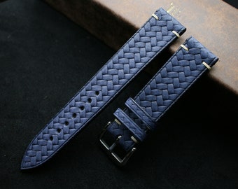 Könnte beinhalten: Zwei blaue Lederarmbänder mit gewebtem Muster. Die Armbänder haben weiße Nähte und werden auf einer braunen Oberfläche gezeigt.